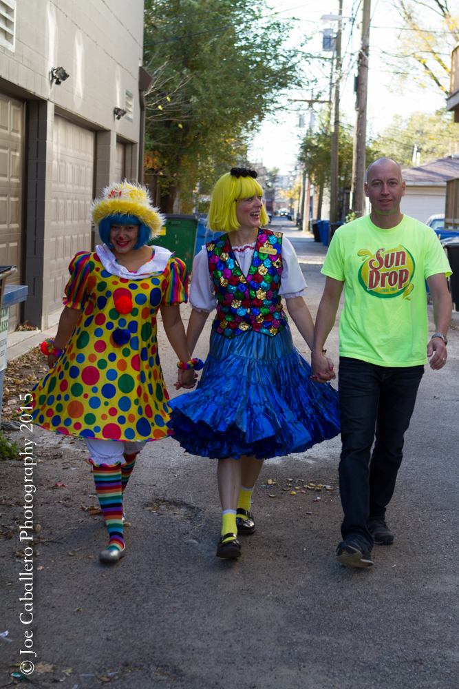 Three people in clown costumes walking down a street.