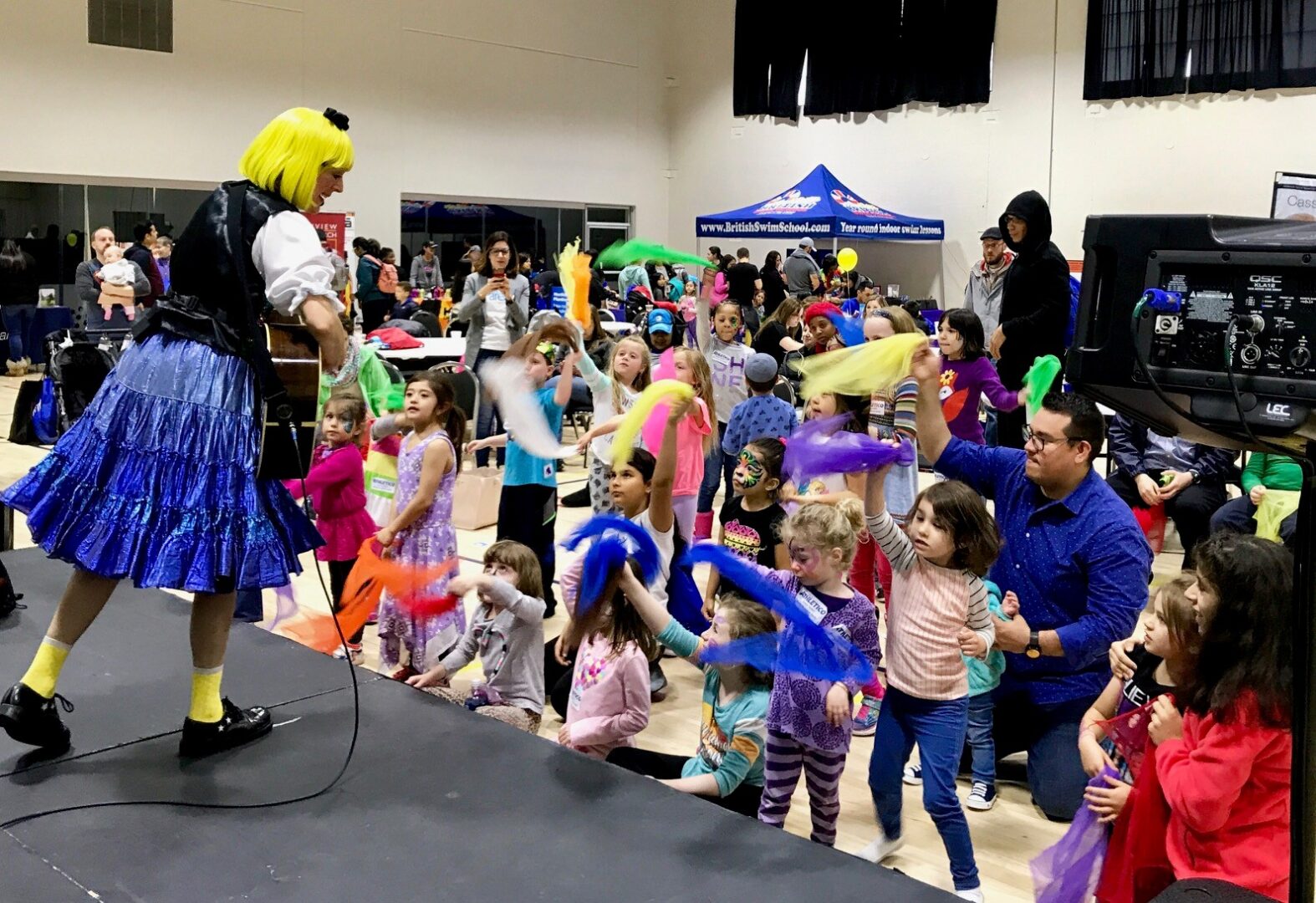 A group of children and adults dancing around with a clown.