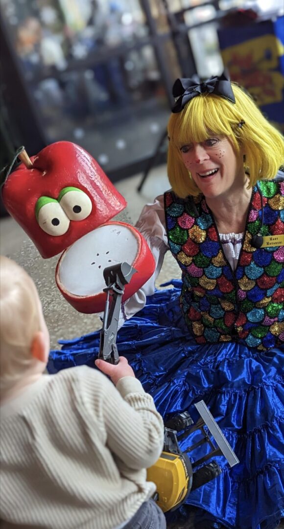 A woman in costume holding an apple while sitting next to a child.